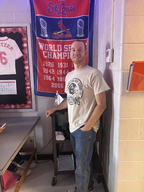 Mr. Keutzer standing next to his cardinals poster in his classroom